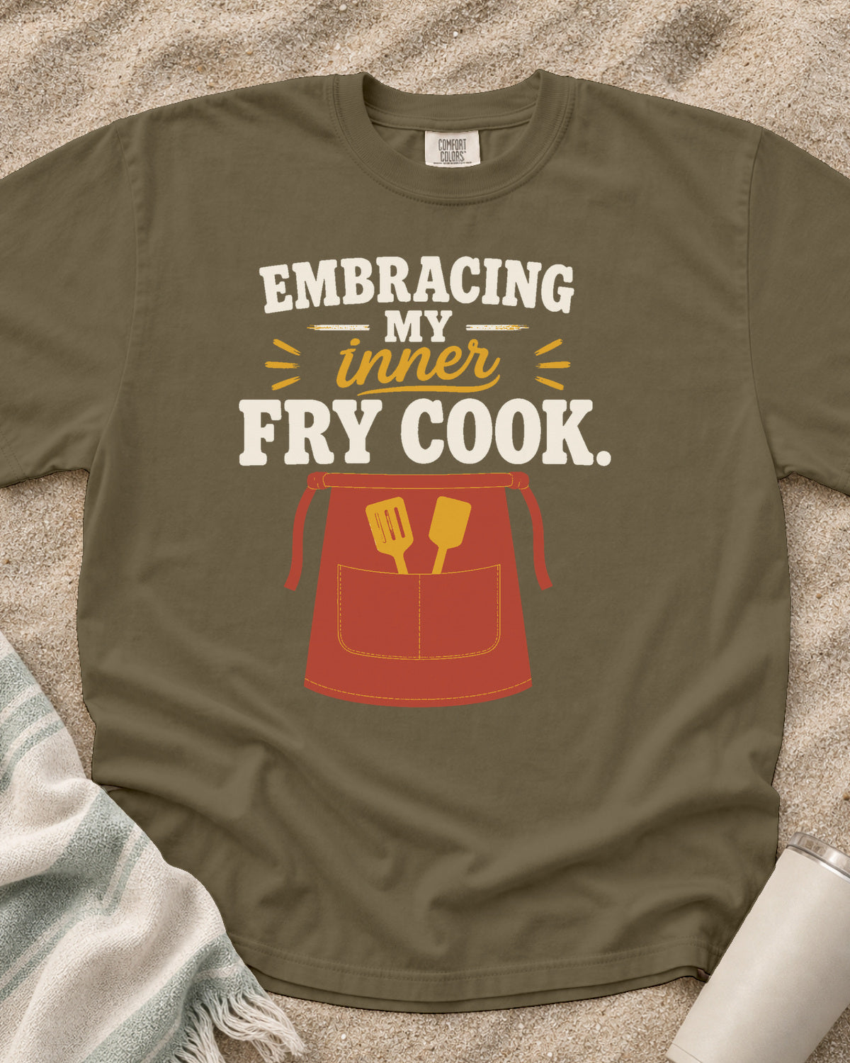 Khaki garment-dyed tee with Embracing My Inner Fry Cook griddle graphic.